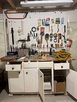 Overall view of pegboard with hand tools, extension cord, workbench cabinet