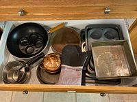 Drawer view showing fry pan, poacher insert, copper kettle, saucepans, square pan, loaf and muffin tins, oven mitt