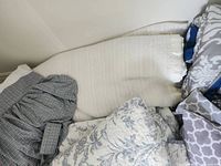 Pile of various patterned bedding including off-white coverlet, plaid sham, floral sham and gray damask pieces