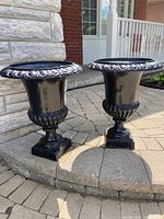 Both black cast iron urn planters on stone walkway showing exterior condition