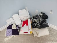 All linens grouped in corner: white towels, Canadian flag towel, crochet throw, beige blanket, Sunbeam heated blanket with controls
