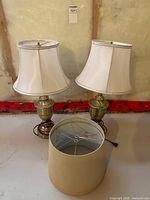 Two brass lamps with white shades and additional beige drum shade
