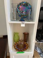 Shelf view showing most pieces: iridescent pedestal compote and plate, clear vases, green vase, copper vase, golden plate