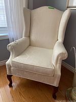 Full view of cream wingback chair showing upholstery and wooden legs