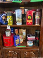 Overall view of top and middle shelves showing multiple branded tins including Planters, Ritz, Baileys, scenic tin