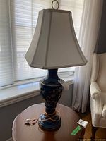 Full view of lamp on side table showing ceramic floral base, white shade and cord