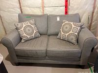 Full view of gray loveseat with two medallion pillows