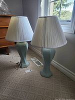 Two matching light blue ceramic table lamps with pleated white shades on carpet