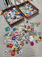 Two shallow boxes and additional loose assortment showing the full quantity and variety of pin-back buttons