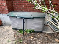 Full exterior view of beige and green Rubbermaid deck box against brick wall