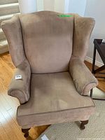front view of tan upholstered wingback chair showing overall design and wear