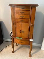 front view of wooden jewelry armoire showing drawers, side doors, lower drawer, cabriole legs