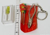 Overall view showing packaged red pouch containing two screwdrivers and pliers keychain alongside separate boxed yellow screwdriver with ruler for scale
