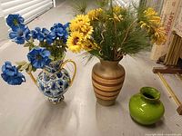 Three vases grouped: blue floral jug with blue flowers, tan striped vase with yellow flowers, small green vase