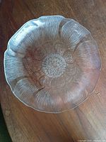 Top view of single clear pressed glass plate showing floral textured pattern and scalloped edge