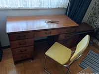 Top view of wood veneer desk, yellow chair, portion of media stand
