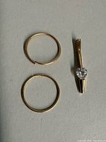Two gold hoop earrings and one gold belly button ring with heart stone
