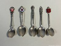 Five souvenir spoons side by side showing size, designs, tarnish