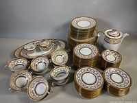 Group shot of entire 77-piece porcelain dinner service showing platters, plates, bowls, cups, coffee pot, sugar bowl, and creamer