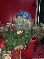 Red tote holding evergreen swags, blue ornament bag visible