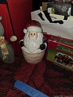 Santa ceramic cookie jar beside red storage bin and gift bag