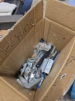 Cardboard box containing assorted metal brackets, hinges and hardware