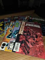 Stack of nine Spider-Man comic books on table, front cover titles visible