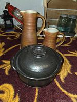 All three items grouped: two brown stoneware pitchers and black bean pot with lid