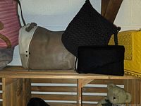 Multiple bags on wooden shelf: suede tote, knit crossbody, velvet clutch, yellow Aldo crossbody partially visible