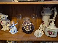 Shelf view showing entire assortment of figurines, glassware, candle, pitcher, soap dispenser