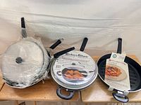 Group shot of five pans, some wrapped, showing Wearever and Kirby & Allen branding and glass lids