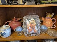 Shelf showing picture frame, teapots, sugar jar, shakers and dishes