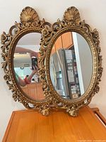 Front view of both ornate oval mirrors showing gold gilded frames and reflective glass