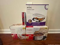 Group of four boxed kitchen items including Rival sandwich maker and Sandra Lee cookware