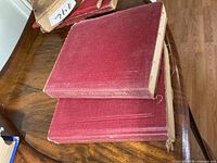 Two red cloth manuals stacked, cloth fraying visible