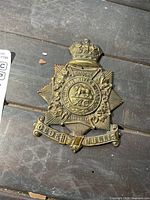 Front view of brass badge showing crown, buffalo emblem, text, motto scroll