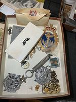 Overview of tray containing badges, buttons, scale, booklet, pins and earrings