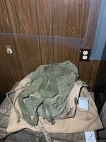 Pile of green backpack and tan tent bag on crate