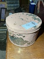 Side view of round metal hat box showing peeling paint and latch