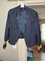 Full front view of navy uniform jacket on hanger showing overall style and gold cuff stripes