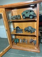 All items displayed in cabinet: jeeps, trucks, armoured car, gun emplacement, three cannons