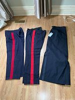 Two navy wool pants with red stripe and one navy skirt laid flat on floor