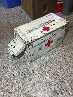 Front view of worn metal Red Cross box showing latch and emblem