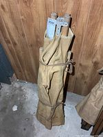 Folded cot standing upright against wall with canvas wrap and lot tag visible