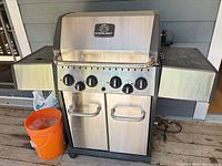 Front view of Sterling propane grill showing stainless body, control panel with four knobs, double-door cabinet, side shelves, casters