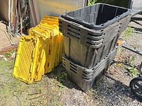 Stack of yellow lids with nested black totes beside shed