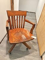 Front angled view of wooden swivel desk chair showing slatted back, armrests and casters