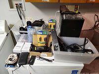 Overall view of lot showing cords, speaker subwoofer, control pod, clock and boxed items
