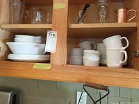Cabinet shelf with Corelle plates, bowls, ramekins, mugs, glassware visible