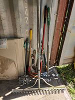 Group of long-handled garden tools leaning against wall